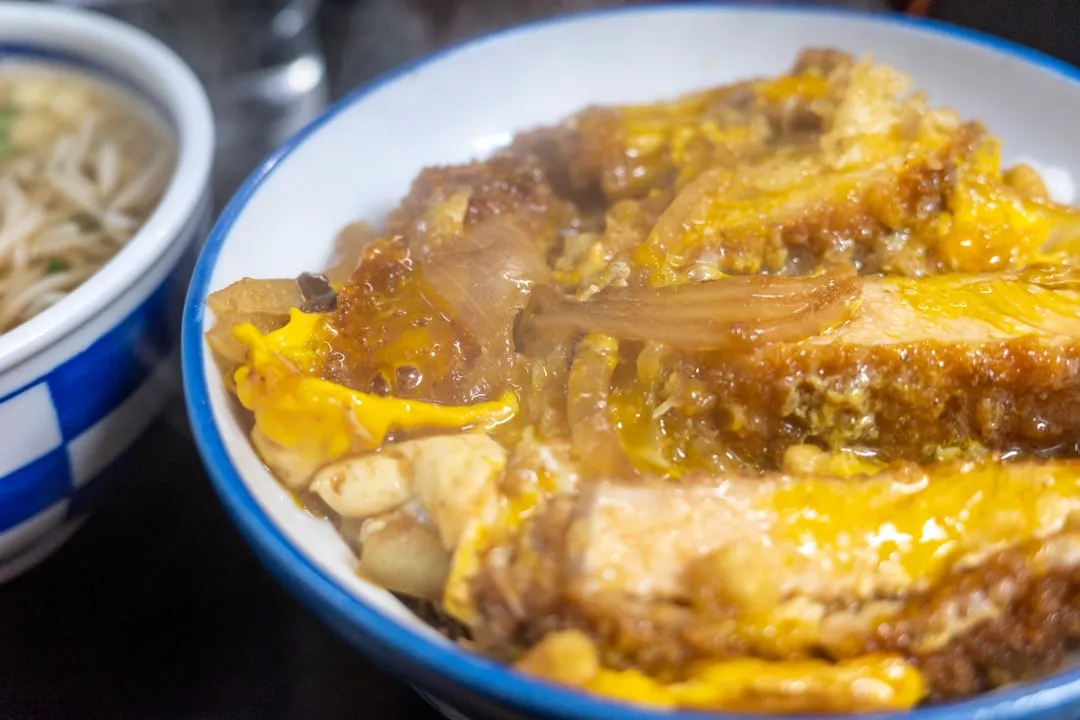 A breathtaking close-up photo of a golden-brown Japanese pork cutlet, perfectly fried with a crispy exterior and juicy interior, glistening with oil on a traditional Japanese plate.