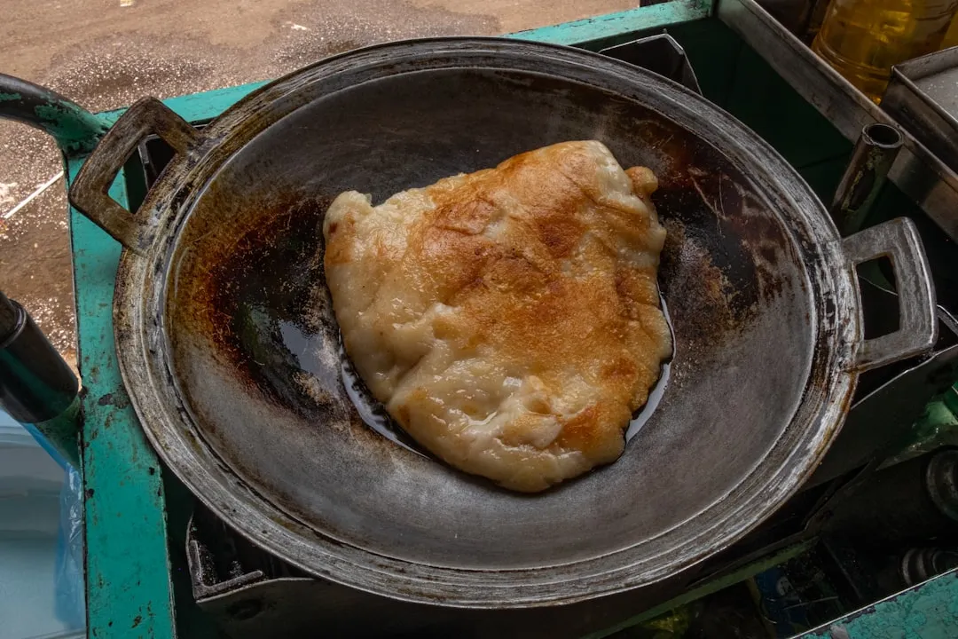 A close-up photo of a golden-brown Japanese street food featuring a perfectly crisped pork cutlet, bathed in a warm glow of streetlights against a backdrop of traditional Japanese architecture.