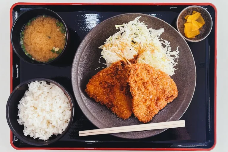 A close-up photo of a perfectly golden crispy pork cutlet, drizzled with savory sauce and resting on a bed of fluffy white rice, capturing the delectable essence of traditional Japanese fried food.