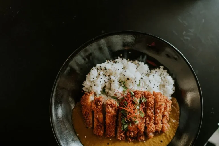 A stunning close-up of a perfectly golden-brown crispy fried pork cutlet drizzled with savory sauce, lying on a vibrant orange paper tray against a backdrop of traditional Japanese street food stalls.