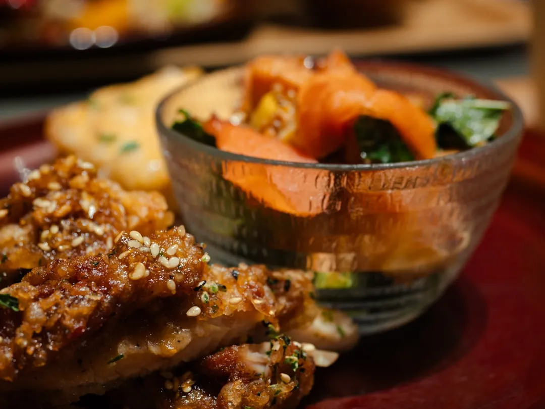 A stunning close-up photo of a golden-brown crispy pork cutlet, seasoned with salt and pepper, drizzled with sweet sauce, resting on a bed of fluffy white rice, in front of a traditional Japanese teacup and chopstick set. Perfect Japanese fried food.