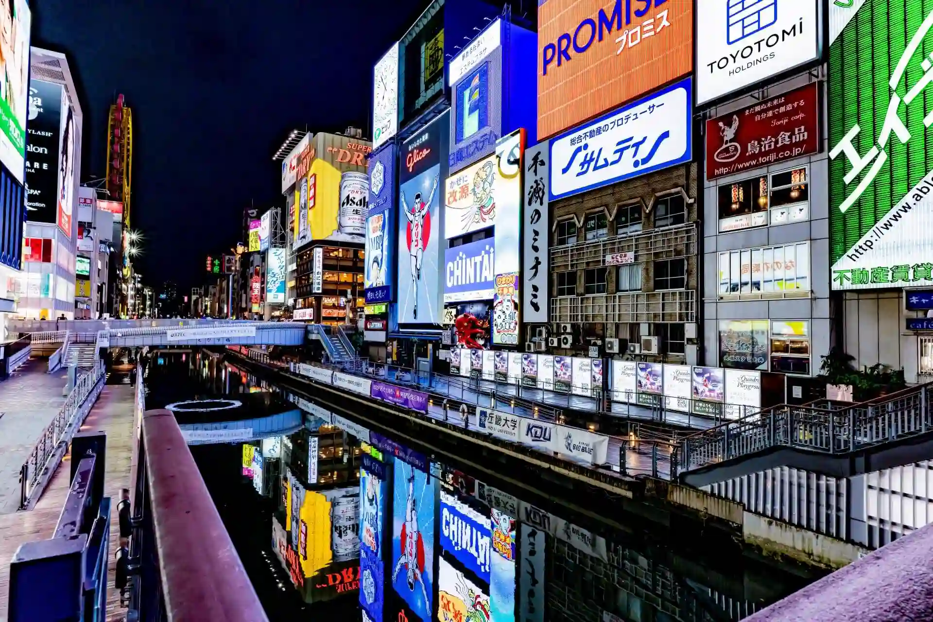 Night view of Dotonbori Canal in Osaka, featuring the famous Glico Running Man sign and vibrant neon lights reflecting on the water.